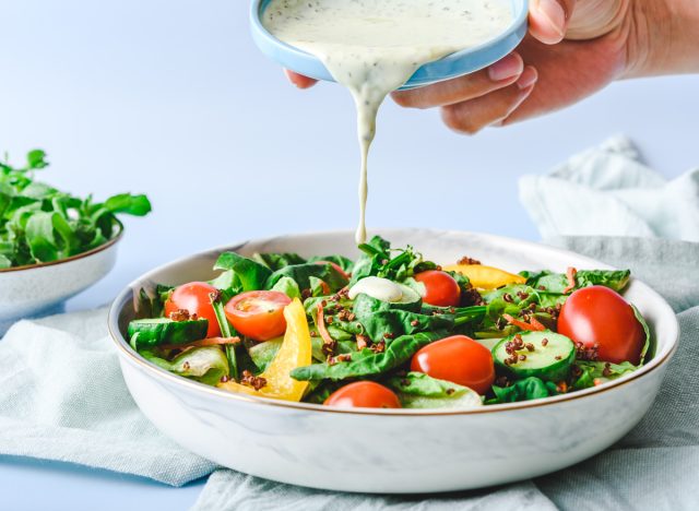 Eine Schüssel mit Salatdressing von Hand auf den Salat gießen
