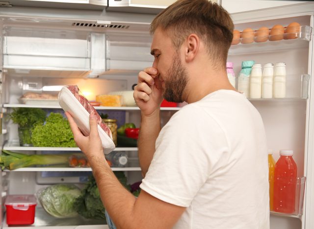 Junger Mann mit schlecht riechendem Fleisch in der Nähe des Kühlschranks in der Küche