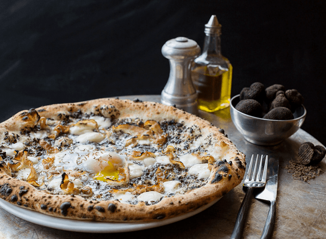a mushroom pizza next to a bowl of truffles and an oil decanter.