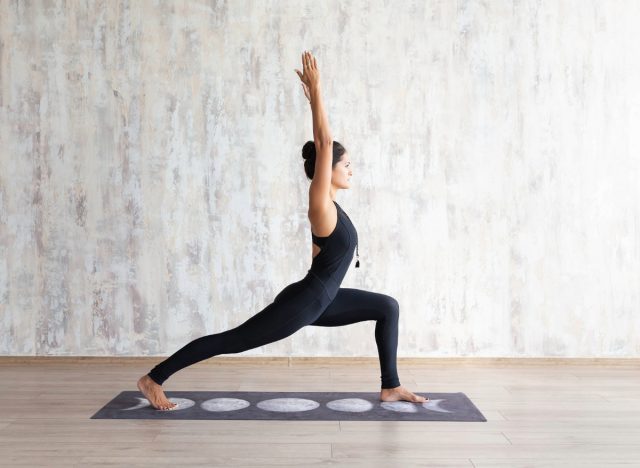 Fitte Frau im schwarzen Strampler macht Yoga-Pose in einem hellen Raum auf einer Yogamatte mit Mondmotiv