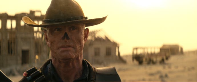 Der Ghul, gespielt von Walter Goggins, steht in diesem Film aus Fallout mit einem Hut vor einer Stadt im Sonnenuntergang.
